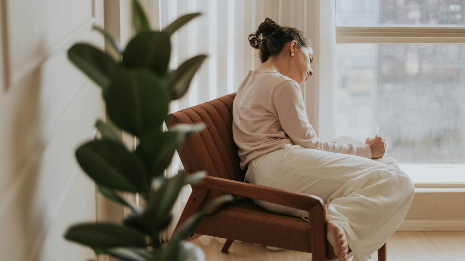 woman sitting by window journaling why do I get upset so easily emotional reflection