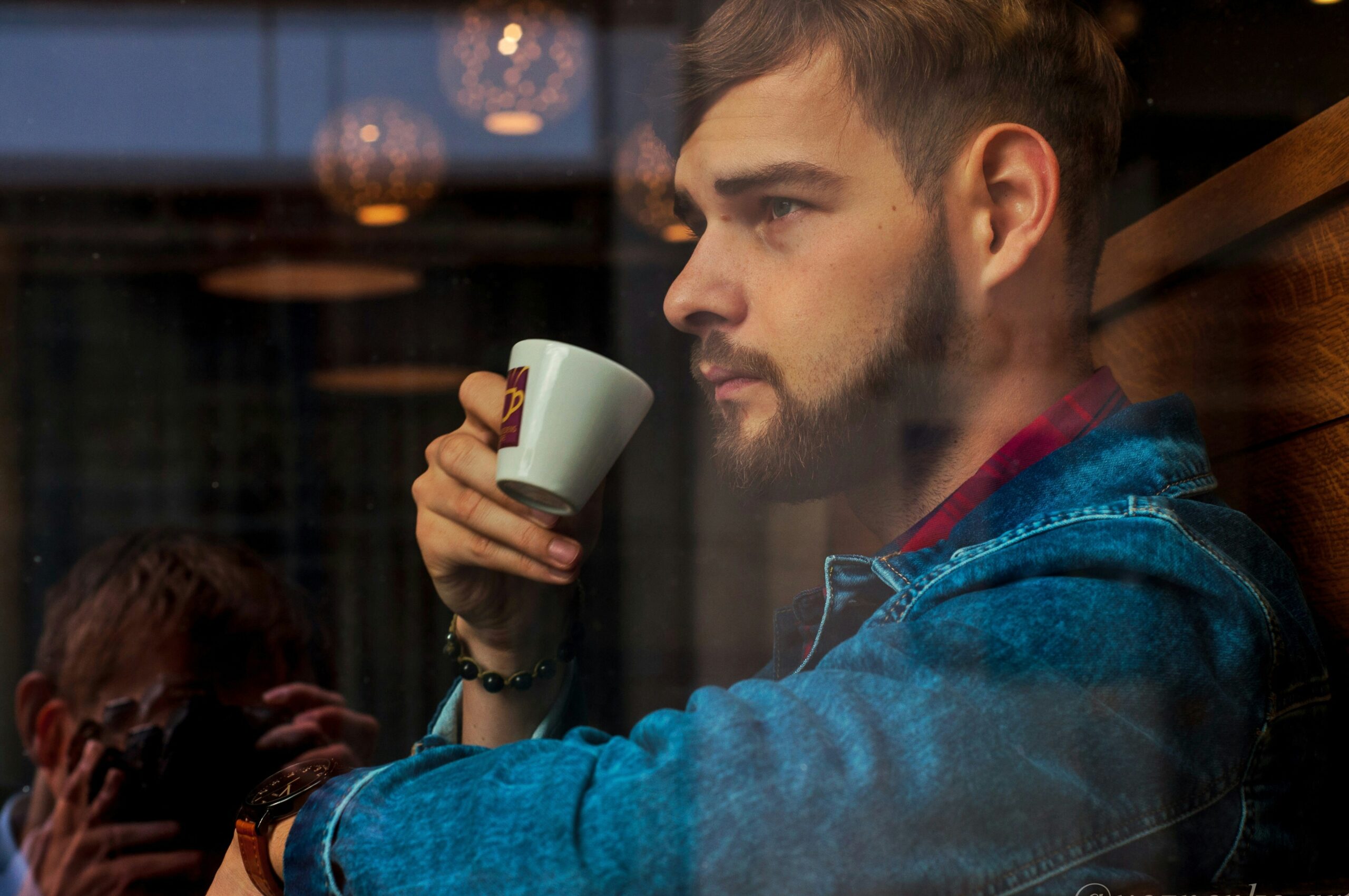 Man sitting in a café replaying conversations in his head and looking thoughtfully out the window